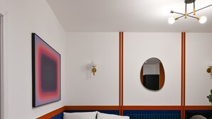 A modern bedroom with a bed, a round mirror, a wall-mounted light fixture, and a framed abstract painting.