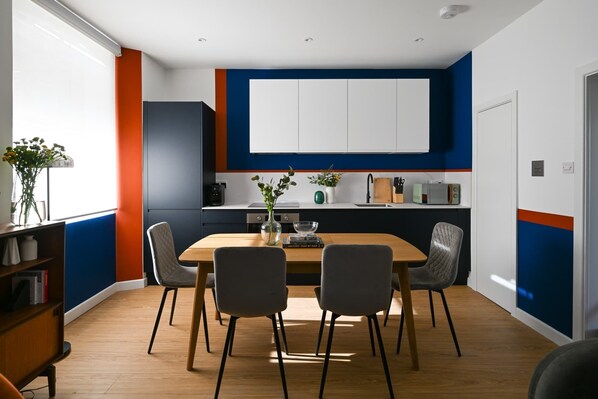 Une cuisine moderne avec des meubles blancs, une table à manger en bois et deux chaises.