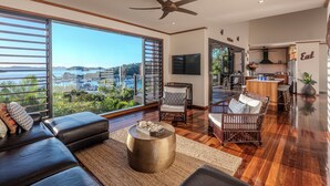 A spacious living room with a large window overlooking a scenic view, a cozy seating area, and a modern kitchen. - Alang Alang, Alang Alang on Hamilton Island (Hamilton Island)