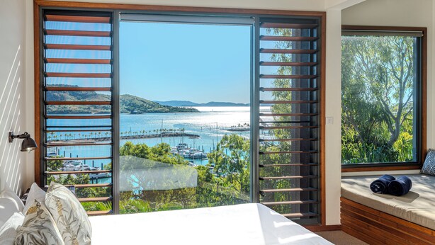 A bedroom with a large sliding glass door leading to a scenic view of a marina and hills. - Alang Alang, Alang Alang on Hamilton Island (Hamilton Island)
