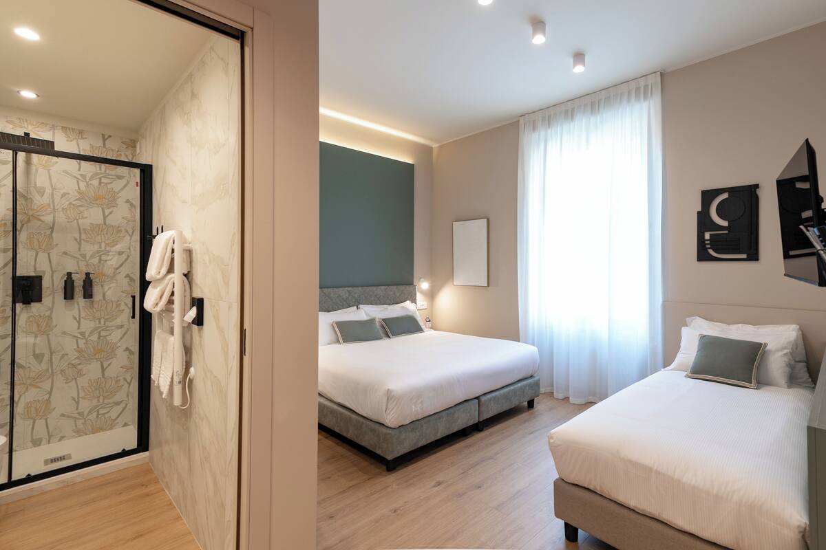 Een moderne hotelkamer met douche, twee bedden en een groot raam met gordijnen.