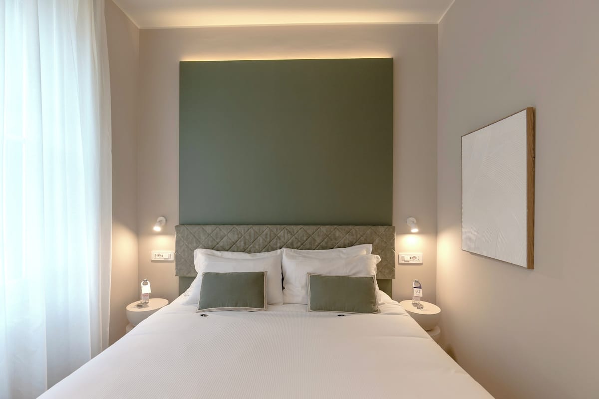 Een keurig opgeruimde hotelkamer met een groot bed, twee nachtkastjes, een hoofdeinde en een kunstwerk aan de muur.