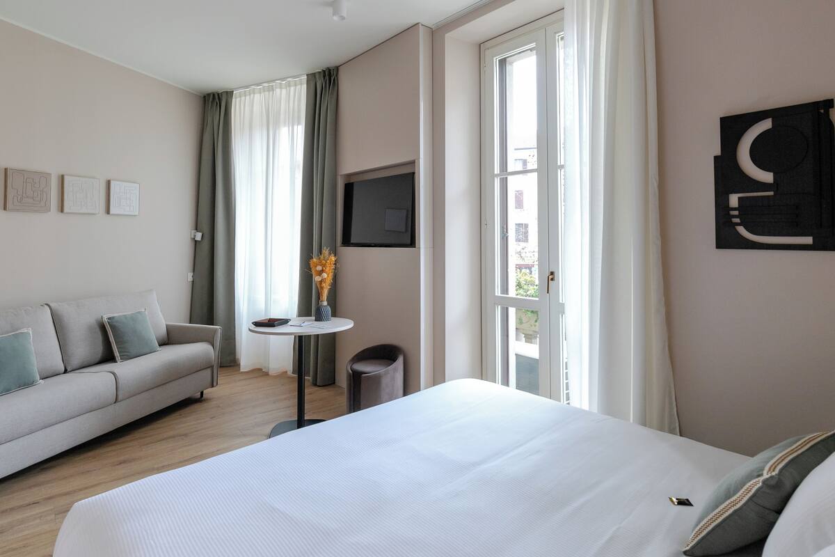 Een moderne hotelkamer met een groot bed, een bank, een klein tafeltje met een vaas en een televisie aan de muur.
