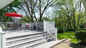 Una terraza de madera con mobiliario exterior, un paraguas rojo y un césped cuidado.