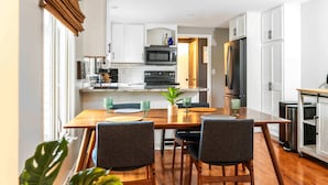 Une cuisine moderne avec des meubles blancs, un réfrigérateur en acier inoxydable et un coin repas comprenant une table et des chaises en bois.
