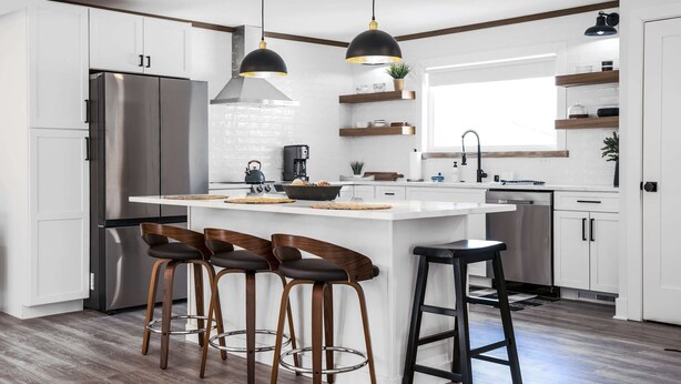 Een moderne keuken met een centraal kookeiland, barstoelen, roestvrijstalen apparatuur en hanglampen.