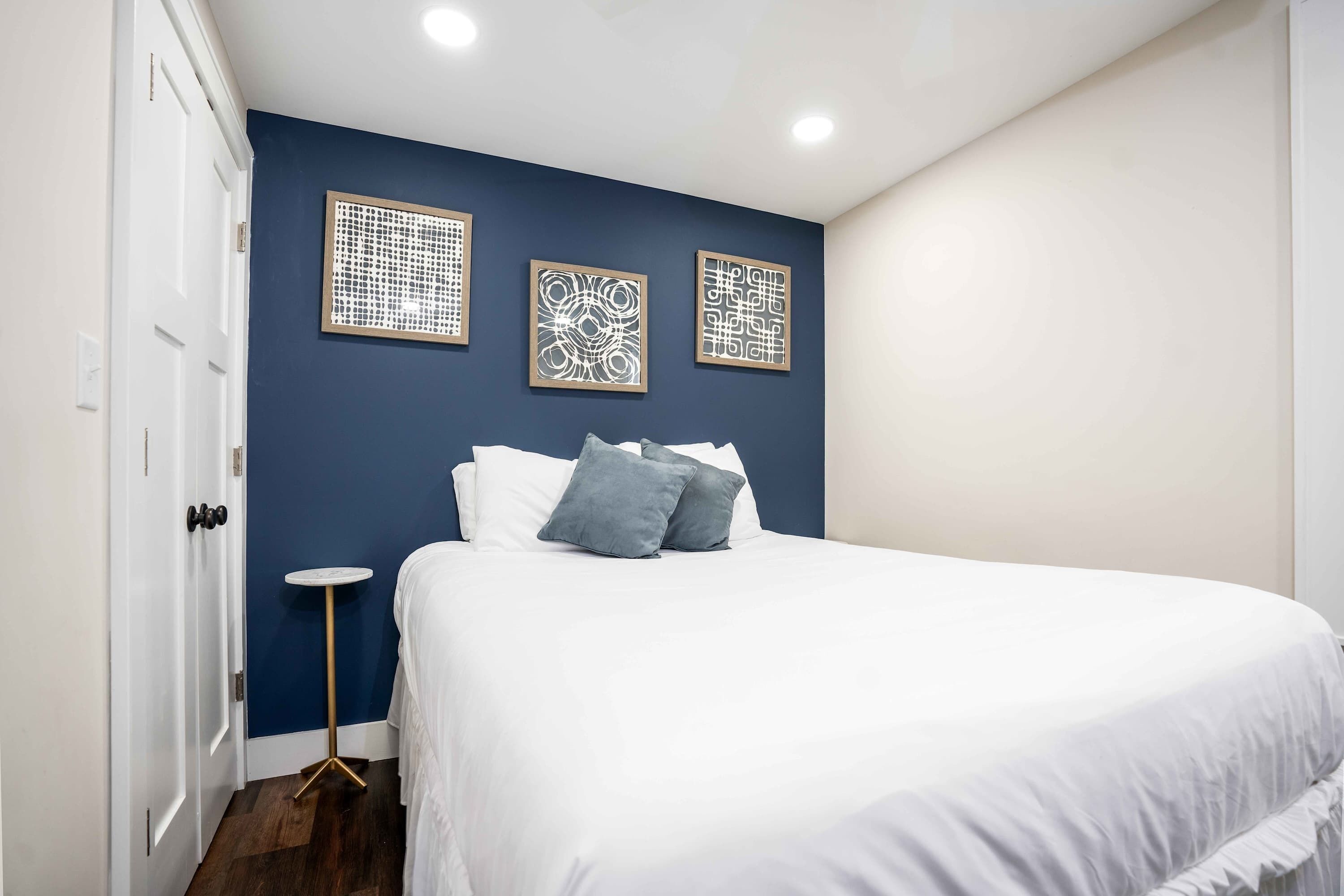 A bedroom with a large bed, a small round table, and three wall art pieces.
