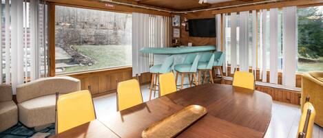 Un comedor con una mesa de madera, sillas amarillas y una zona de bar con sillas color turquesa.