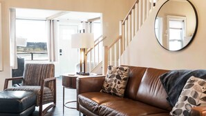 Un salon avec un canapé en cuir, un fauteuil à rayures, une petite table avec une lampe et un miroir au mur.
