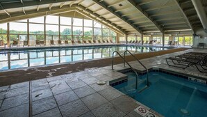 Piscina interna com vista clara para o exterior, chão revestido com azulejos e espreguiçadeiras.