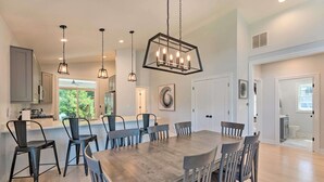A spacious dining area with a large wooden table and multiple chairs, a kitchen with modern appliances, and pendant lighting.