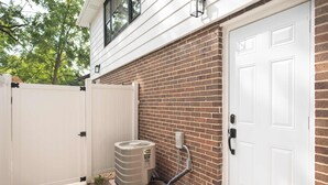 Une façade d’habitation avec un mur en briques, une porte blanche et un appareil de climatisation.