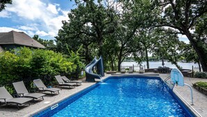 Une piscine avec un toboggan, des chaises longues et une vue sur un plan d’eau.
