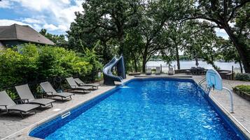 A swimming pool with a slide, lounge chairs, and a view of a body of water.