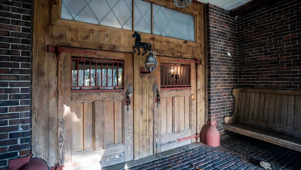A wooden door with glass panels, a horse decoration, and a bench inside a building with brick walls. - The Hideaway at Hayloft Lodge – Chic & Unique Stay (Lake Geneva)