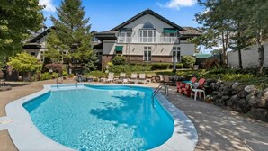 A swimming pool with lounge chairs, a stone wall, and a two-story building in the background. - The Hideaway at Hayloft Lodge – Chic & Unique Stay (Lake Geneva)