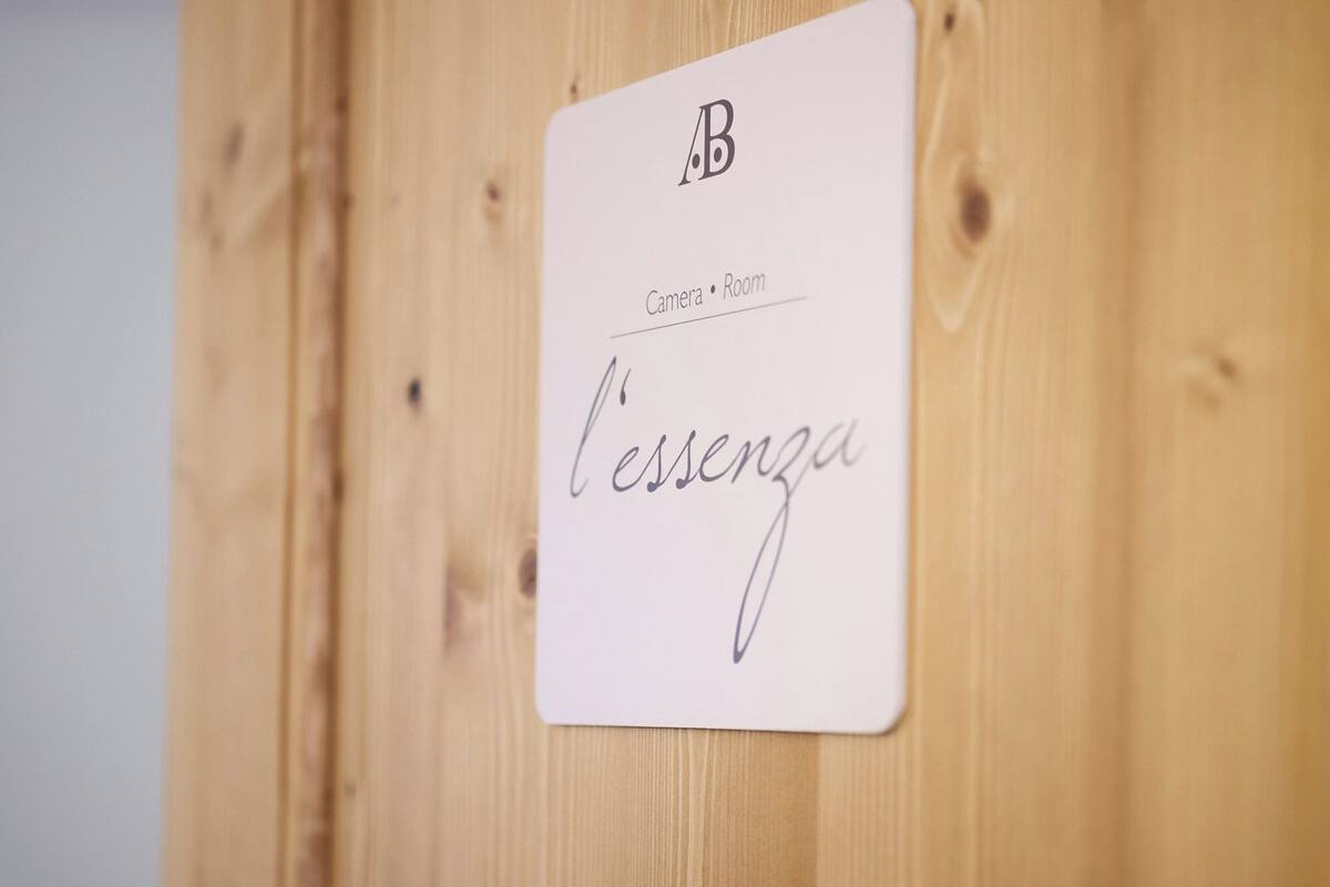 Ein Schild mit der Aufschrift 'Camera Room' und 'l'essenza' vor einem Holzuntergrund.