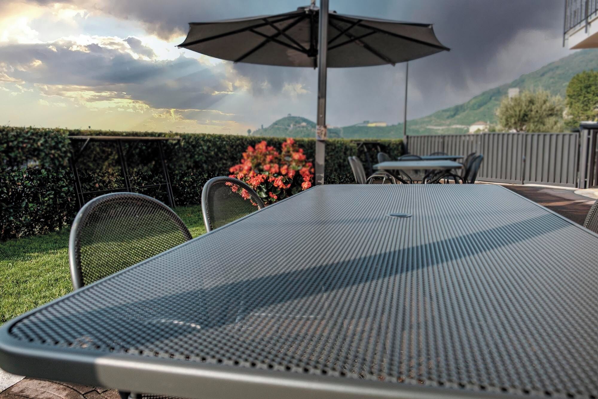 Eine Terrasse mit einem Metalltisch und Stühlen, einem Sonnenschirm und Blick auf eine gebirgige Landschaft.