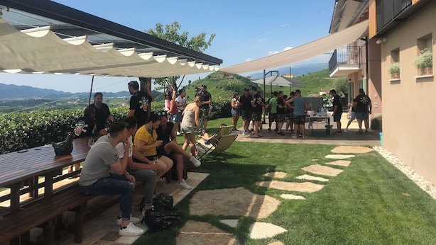 Un patio exterior con bancos y mesas de madera, rodeado de un césped cuidado y vistas a colinas distantes.