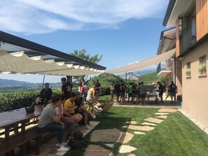 Un patio exterior con bancos y mesas de madera, rodeado de un césped cuidado y vistas a colinas distantes.