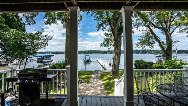 Une terrasse couverte avec un barbecue, des sièges d’extérieur et une vue sur un lac où l’on peut voir des bateaux.
