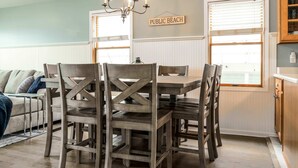Un espace repas avec une table et des chaises en bois, un lustre et une pancarte indiquant « PLAGE PUBLIQUE ».