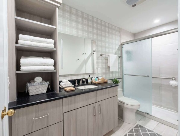 Un baño con cabina de ducha de vidrio, un lavamanos con espejo y un perchero con toallas dobladas.