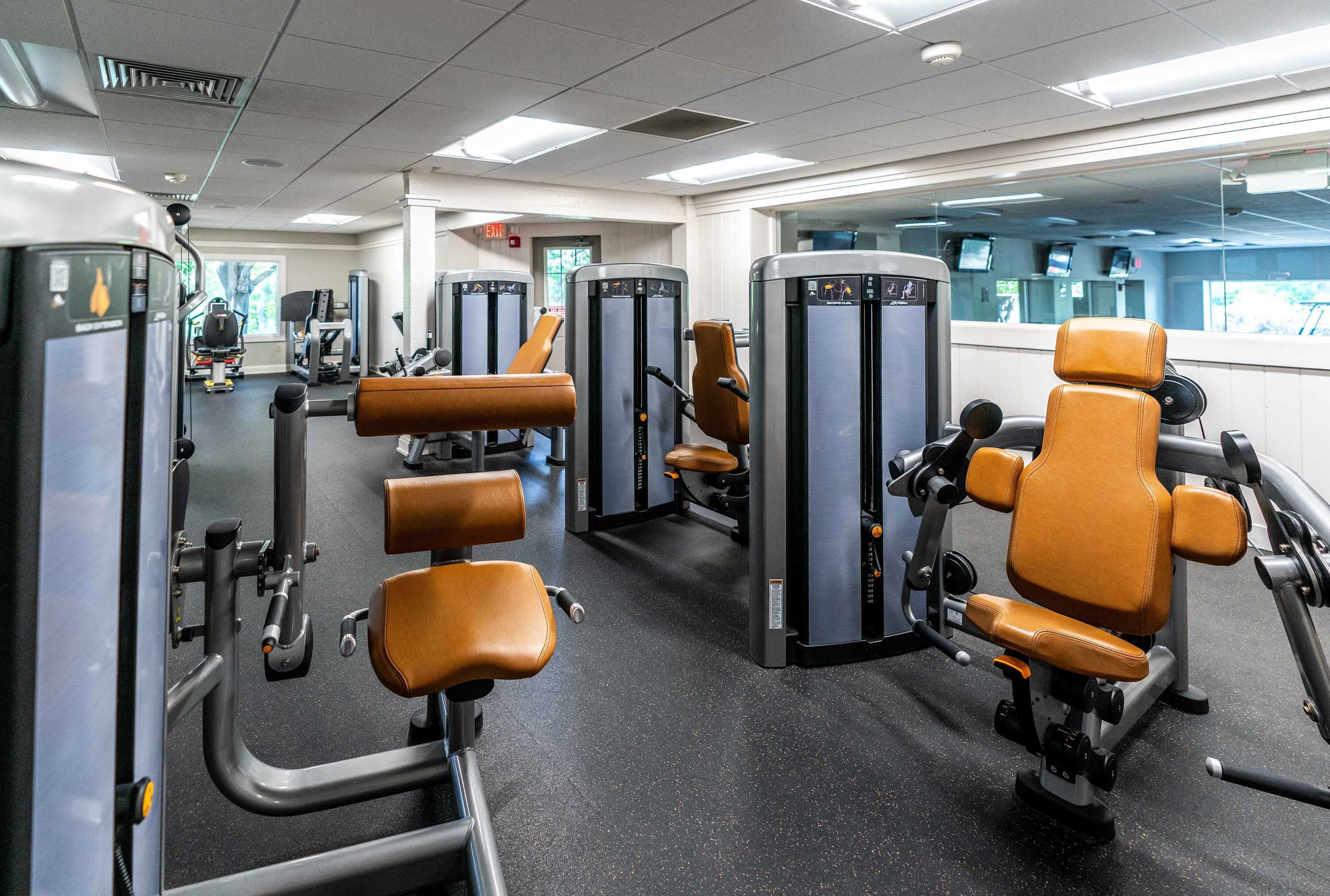 A gym with various exercise machines and brown leather chairs.