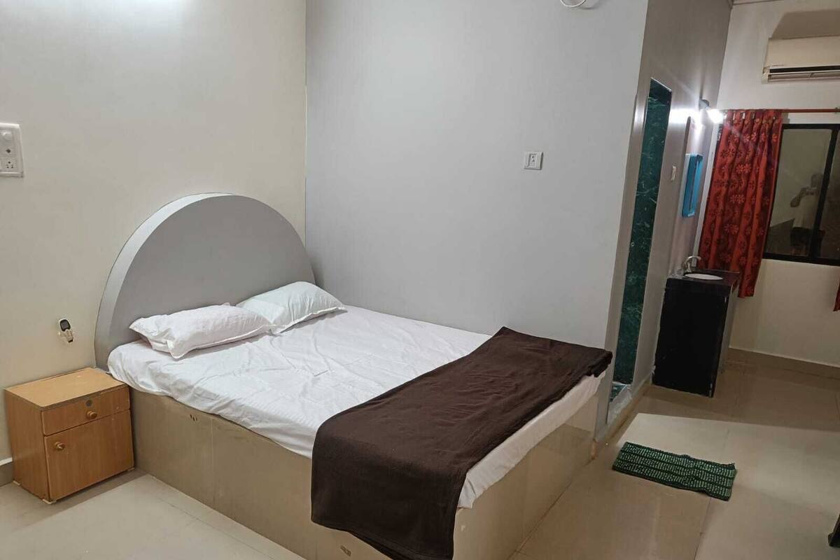 Ein Schlafzimmer mit einem Bett, einem Nachttisch aus Holz, einem Badezimmer mit Waschbecken und Spiegel sowie einer grünen Matte auf dem Boden.