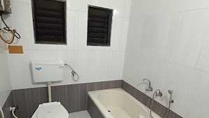 Et badeværelse med toilet, badekar og to vinduer.