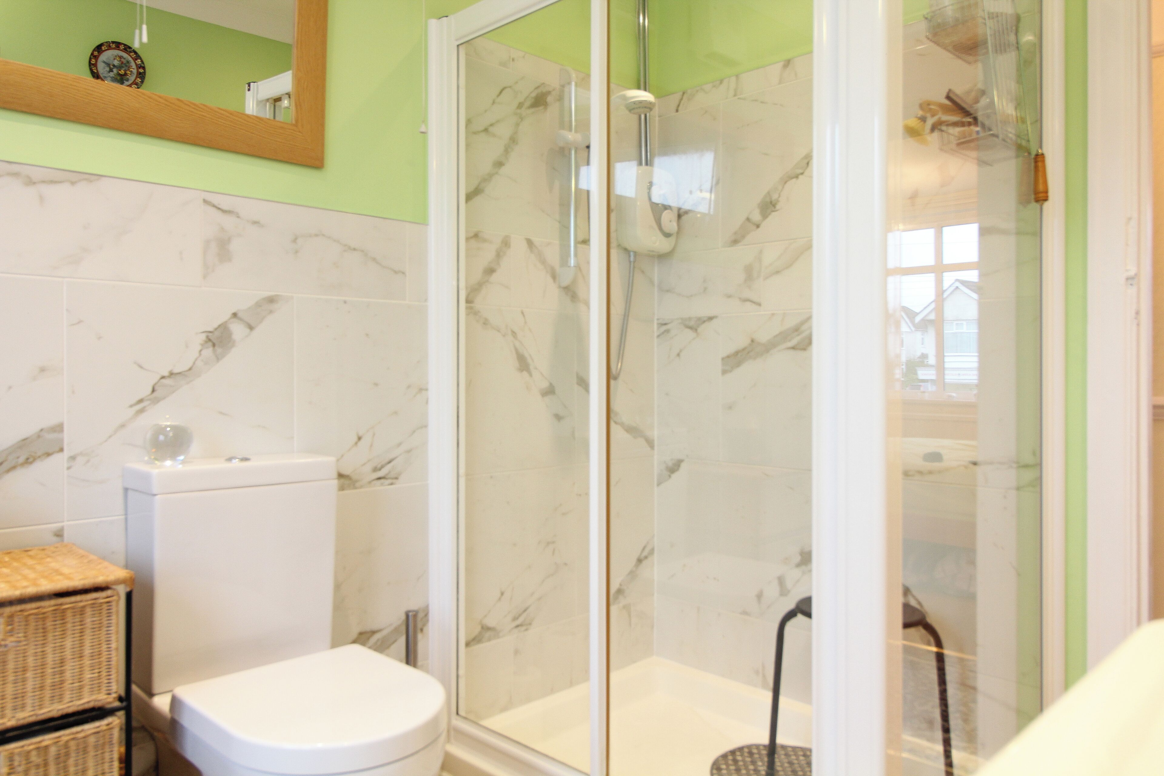 A bathroom with a toilet, a shower with a glass door, and a marble-tiled wall.