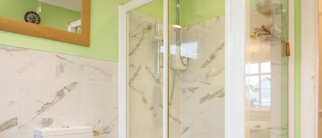 A bathroom with a toilet, a shower with a glass door, and a marble-tiled wall.