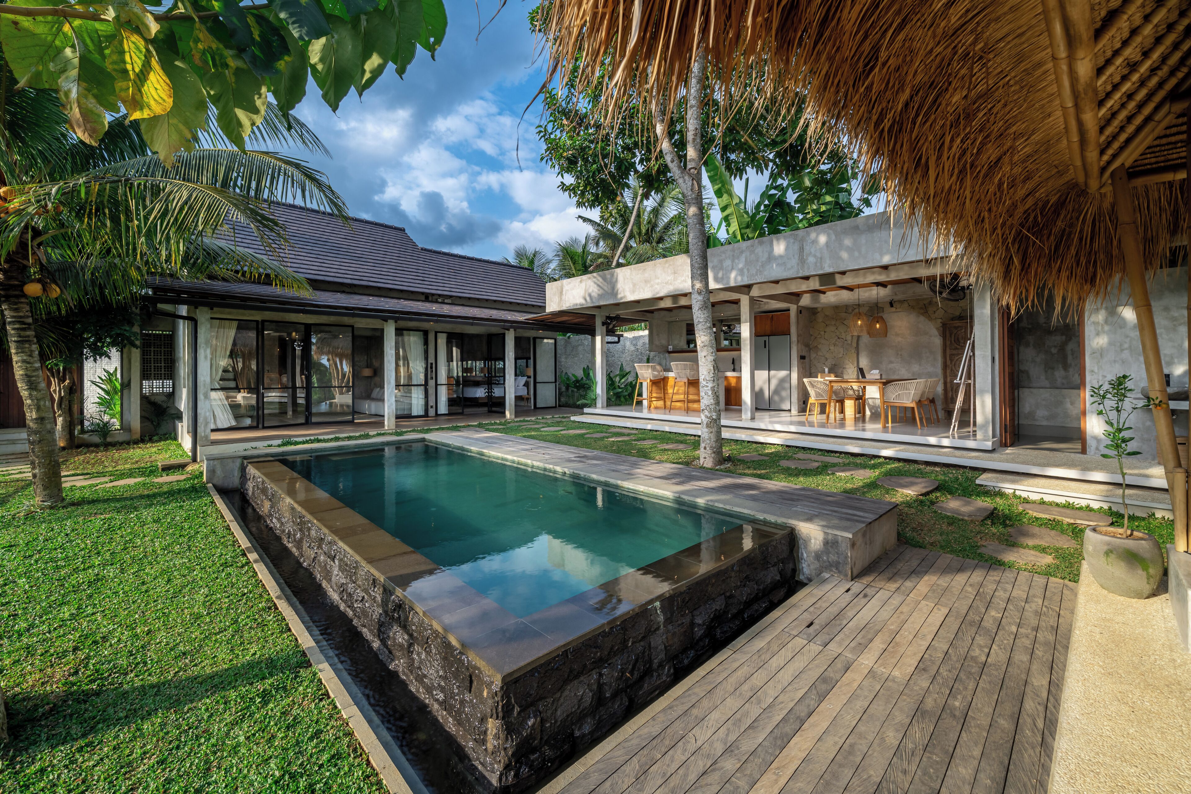 Una casa moderna con piscina, mobiliario de exterior y una estructura de techo de paja.