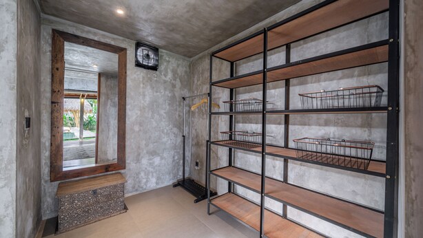 A hallway with a concrete wall, a wooden bench, and a metal shelving unit with baskets. - Sola Villa Ubud - 2 Bedrooms (Ubud)