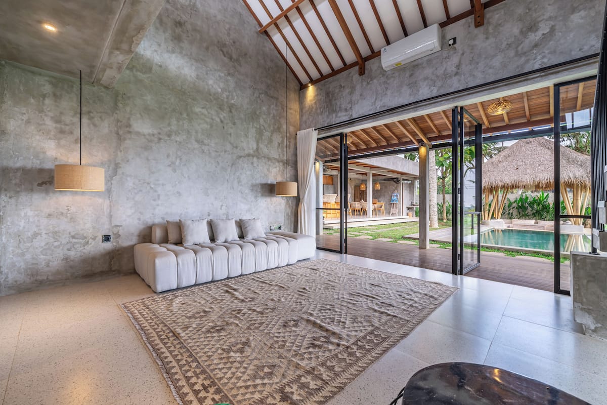 Un salon moderne avec un grand canapé, un tapis à motifs et une vue sur un espace piscine extérieur.