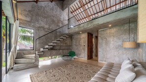 A spacious living area with a high ceiling, a staircase, a sofa, and a large rug. - Sola Villa Ubud - 2 Bedrooms (Ubud)