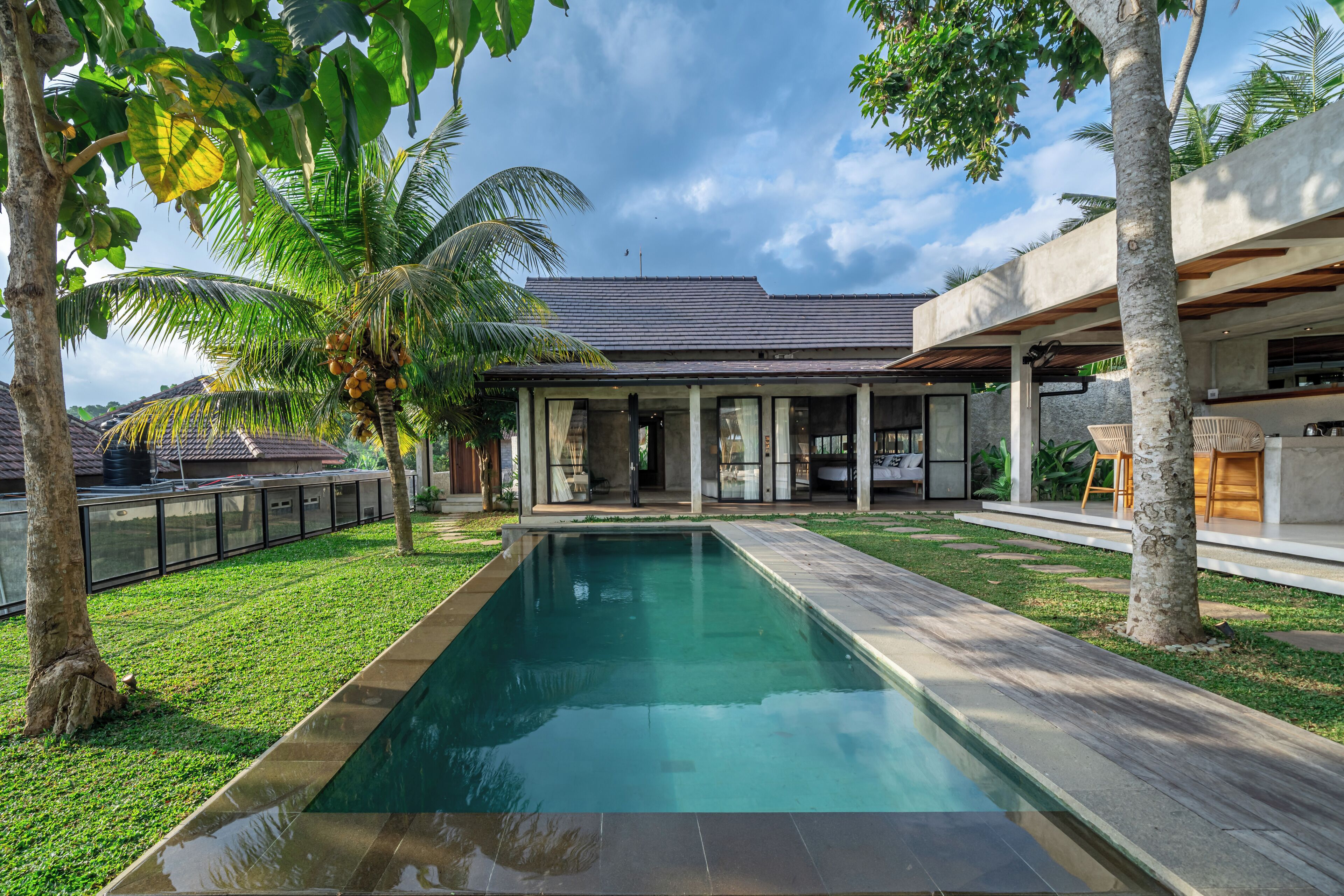 Una casa moderna con piscina, patio cubierto y exuberante vegetación.