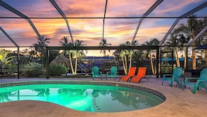A swimming pool with a tiled edge, surrounded by lounge chairs and palm trees. - Serenity by the Gulf - Vesteva Vacation Rentals (Cape Coral)