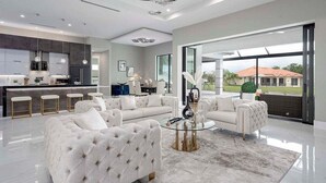 A modern living room with a large sectional sofa, a glass coffee table, and a view of the outdoors through large windows.