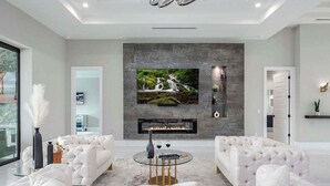 A modern living room with a fireplace, white sofas, and a large TV screen.