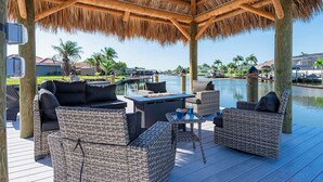 An outdoor patio with wicker furniture, a table, and a thatched roof structure.