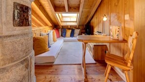 Ein gemütliches Dachzimmer mit Holzbalkendecke, einer Steinpfeiler, einem Bett mit Kissen, einem kleinen Tisch und einem Stuhl.