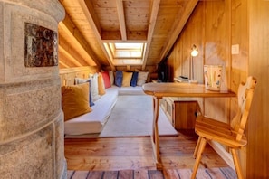 Ein gemütliches Dachzimmer mit Holzbalkendecke, einer Steinpfeiler, einem Bett mit Kissen, einem kleinen Tisch und einem Stuhl.