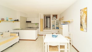 A modern kitchen with white cabinets, a dining area with a white table and chairs, and a hallway leading to a bedroom.