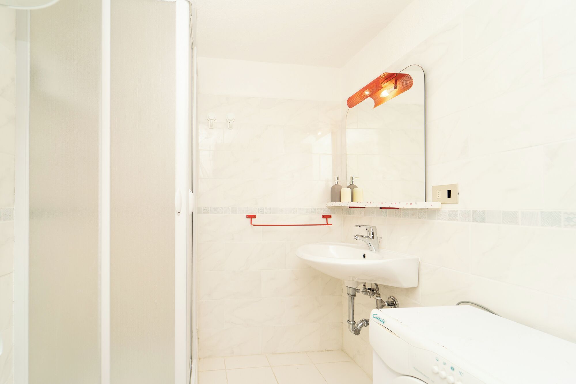 Un baño con lavamanos blanco, un espejo con luz y un toallero rojo.