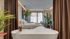 A modern hotel room with a large bathtub, a bed with a view of the city, and several potted plants. - Deo Plaza by Downtown Apartments (Gdansk)