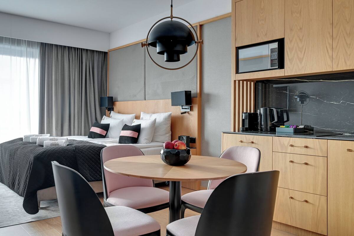 A modern hotel room with a bed, bedside table, and a round dining table with chairs.