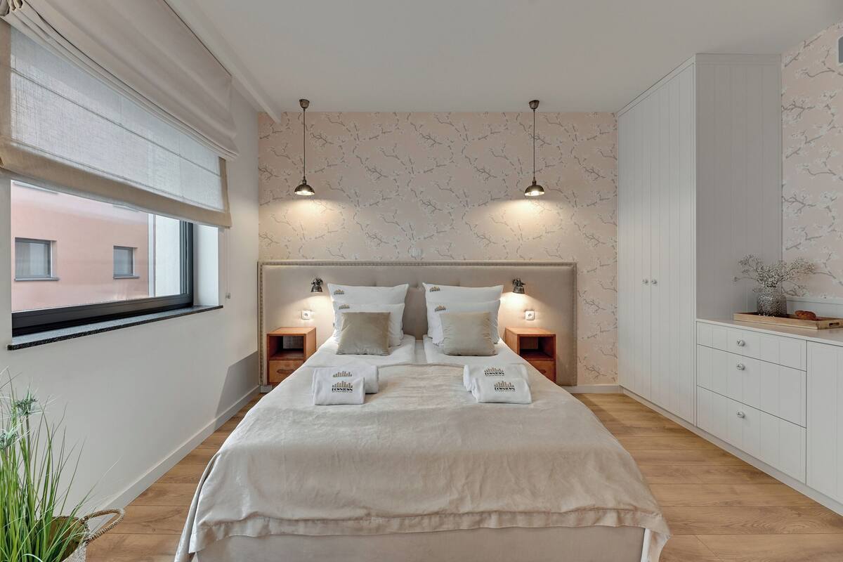 A neatly arranged bedroom with a large bed, bedside tables, and a window with blinds.