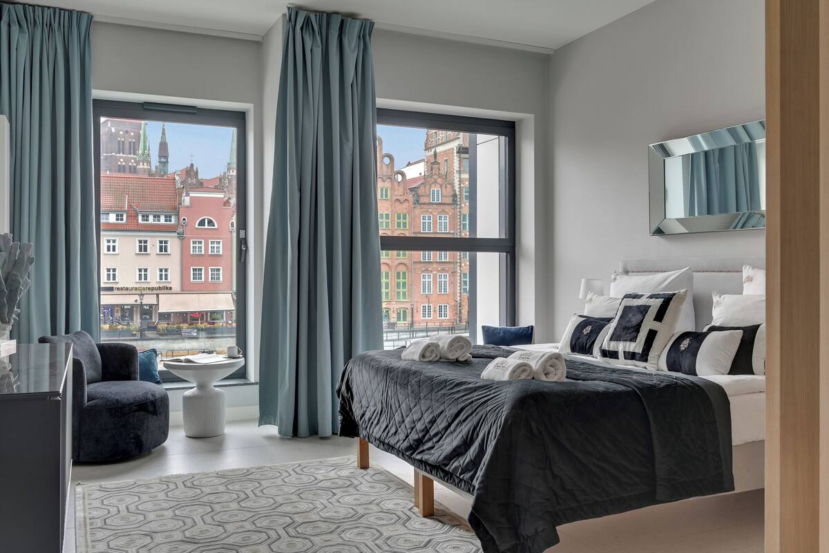 A modern hotel room with a large bed, a view of the city, and a small table with a chair.