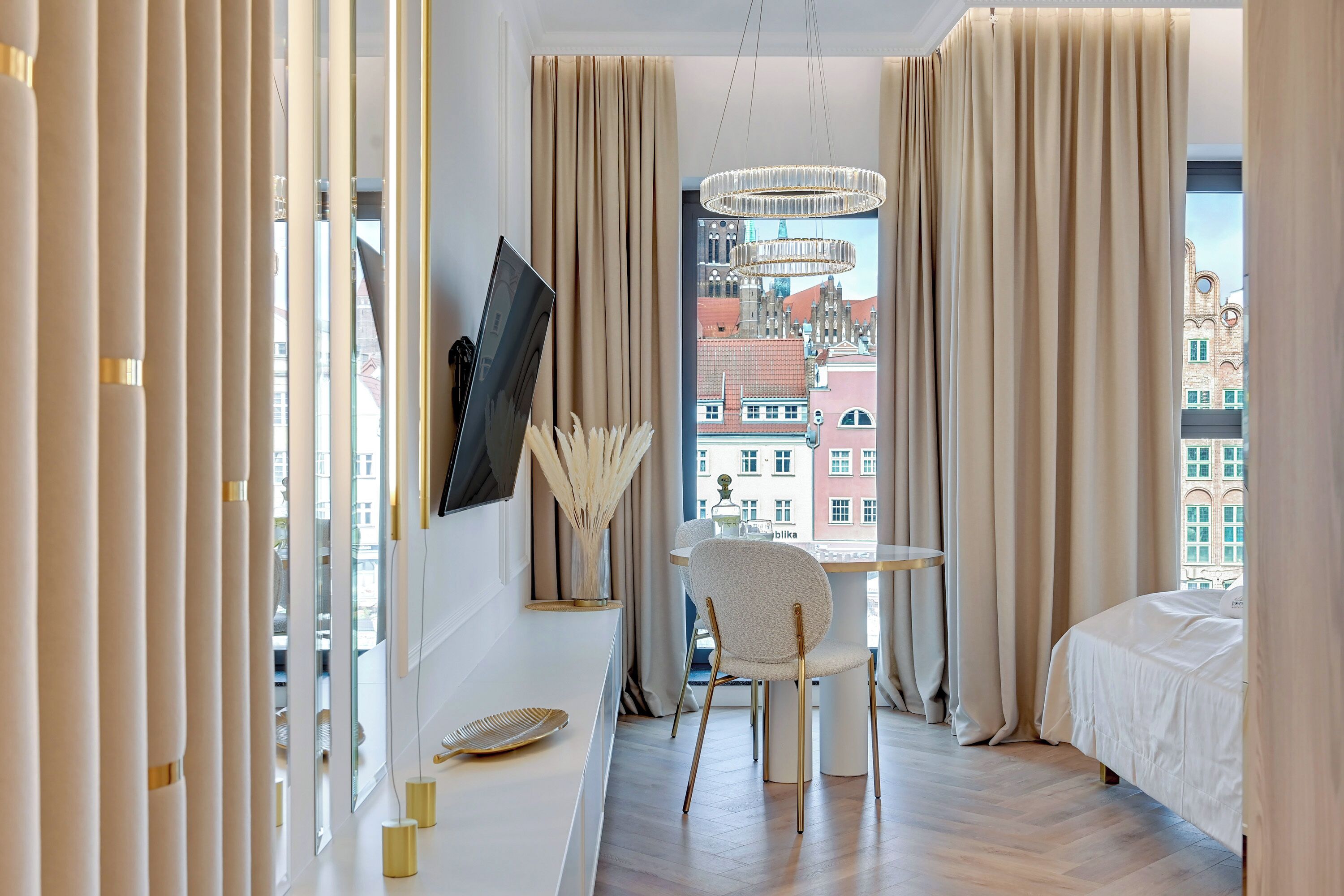 Una habitación de hotel moderna con un ventanal grande, una cama, una mesa de comedor con sillas y un candelabro.